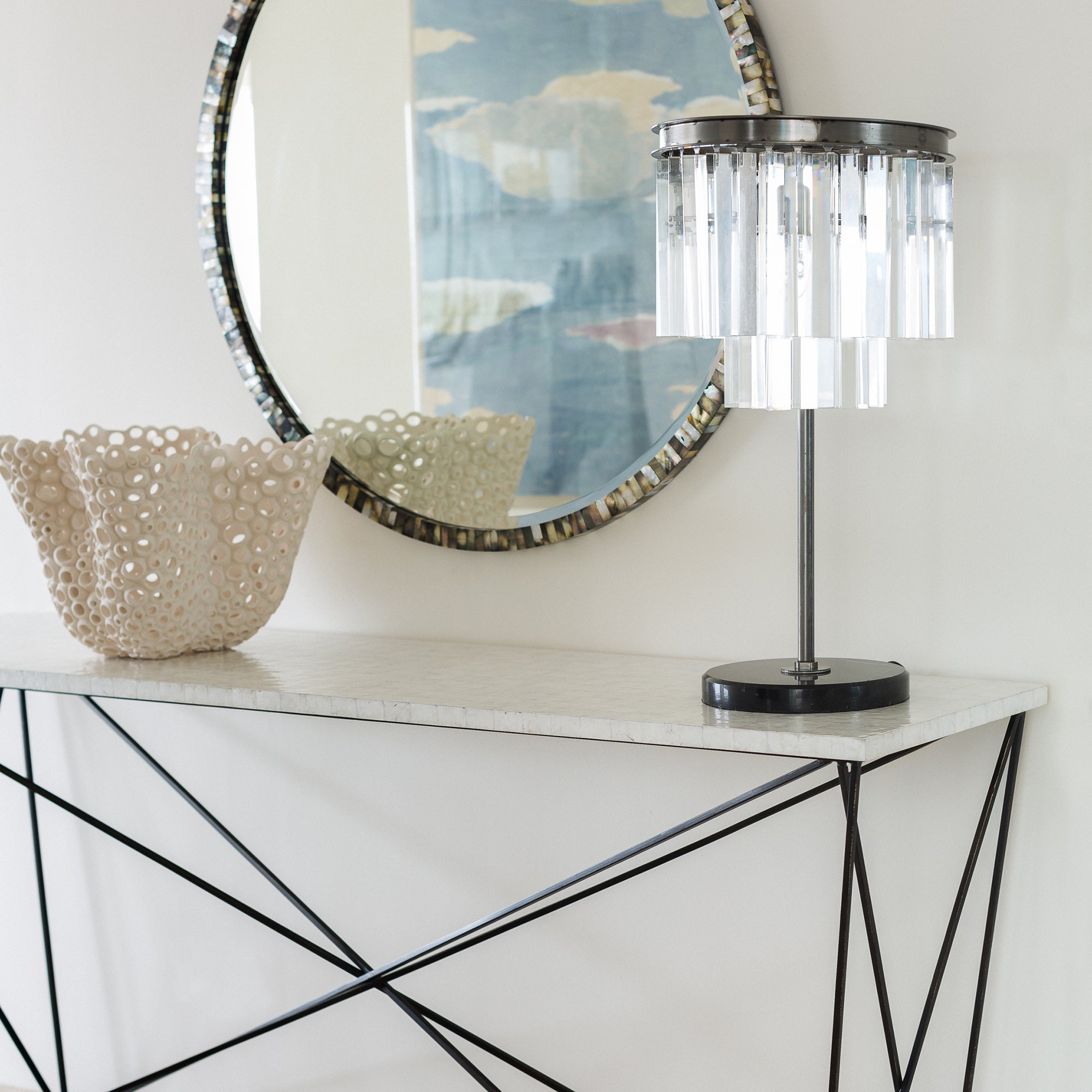 white shell console table styled with decor below round mirror