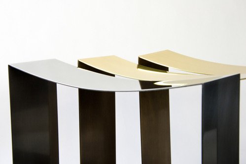 closeup of one steel-finished stool shown with two of the same stools finished in darkened brass
