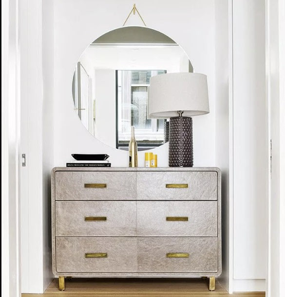 dresser styled in nook with table lamp and round wall mirror